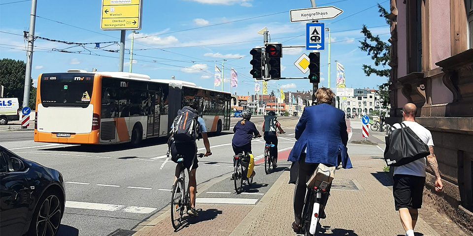 Fahrradfahrer auf einem Radfahrstreifen und auf dem Gehweg an einer großen Kreuzung.