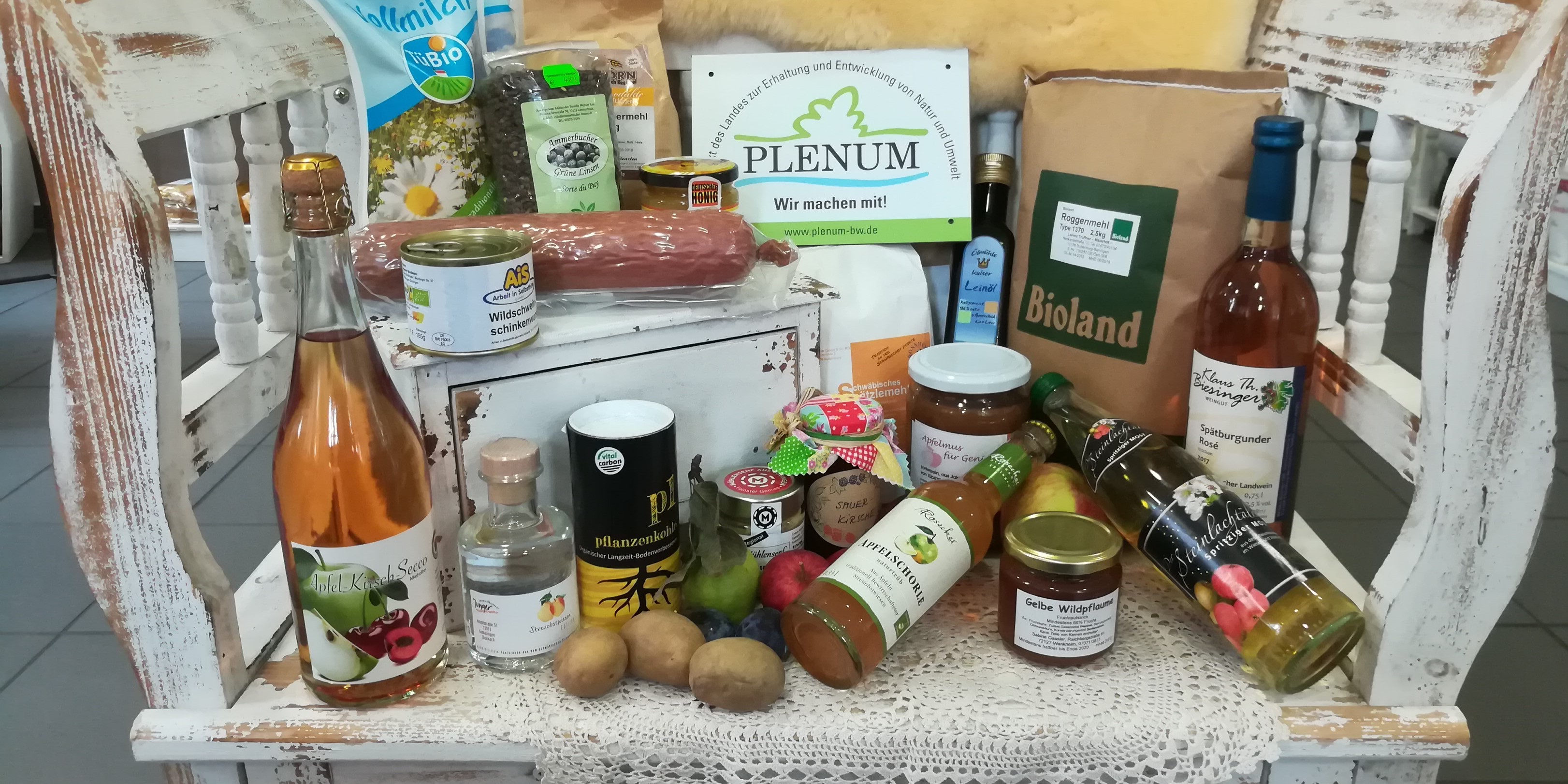 Verschiedene PLENUM-Produkte wie Streuobstsaft, - secco, -most und -marmelade, Linsen, Biomehl, Wurst et cetera werden auf einer kleinen Bank präsentiert.