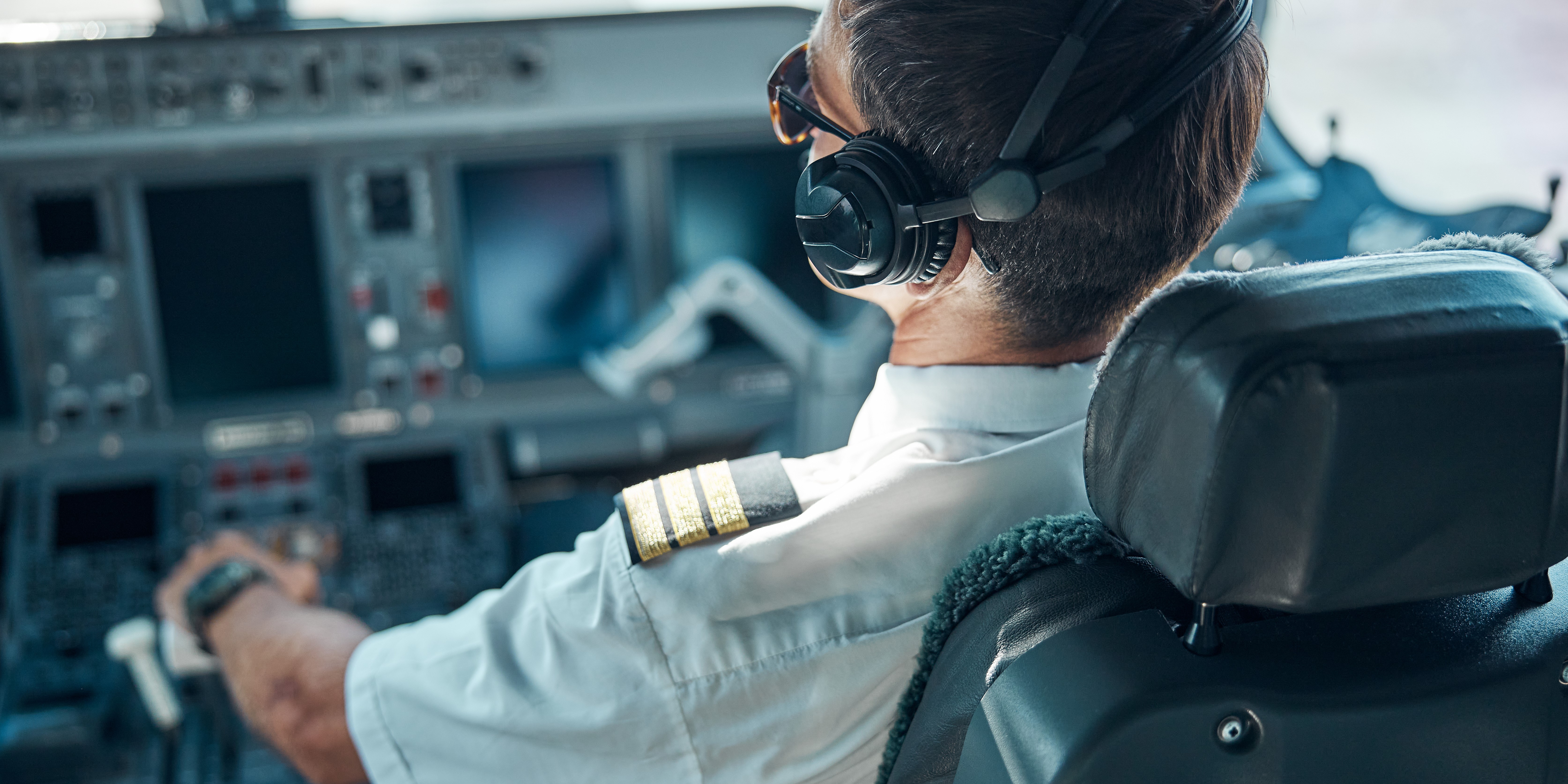 Blick von hinten auf einen Pilot im Cockpit eines Flugzeuges. 