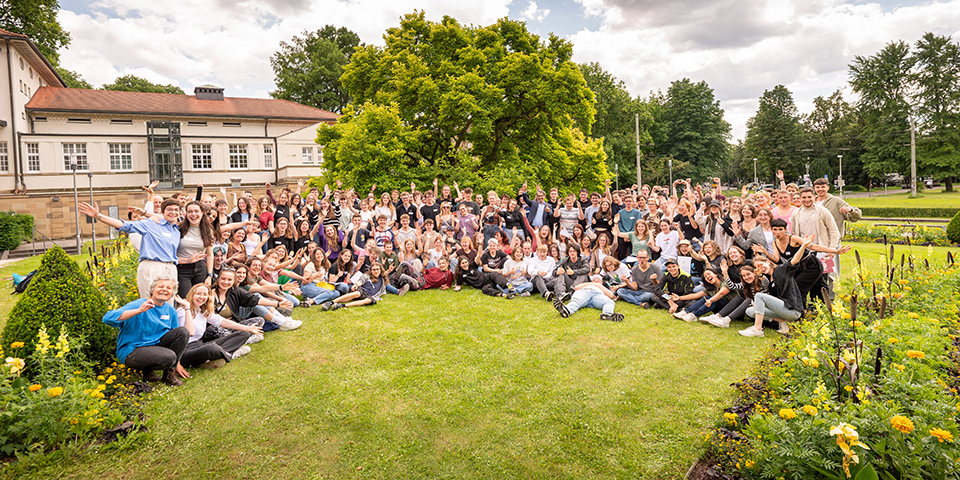 Die teilnehmenden Personen haben sich auf einer Rasenfläche für das Gruppenfoto aufgestellt.