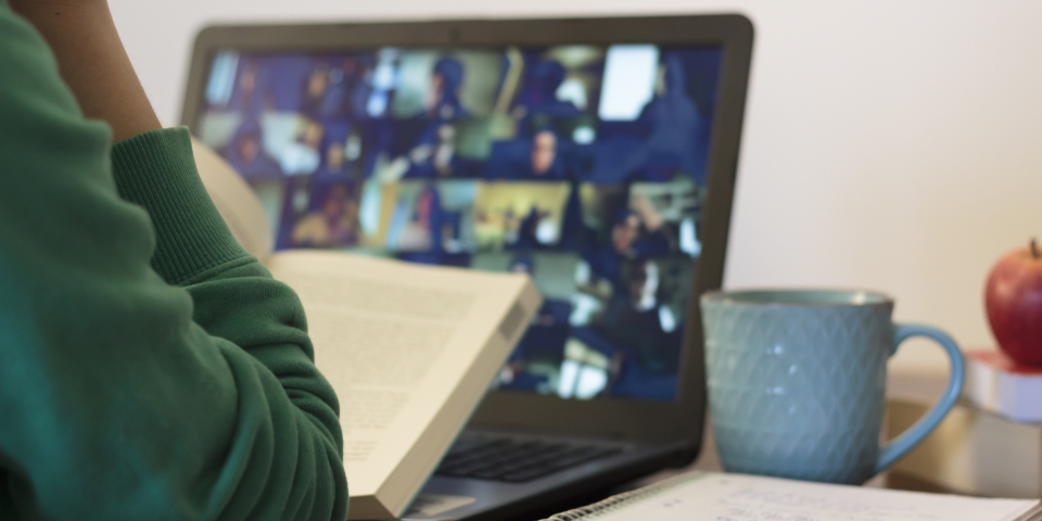 Person sitzt mit Buch vor einem Laptop.