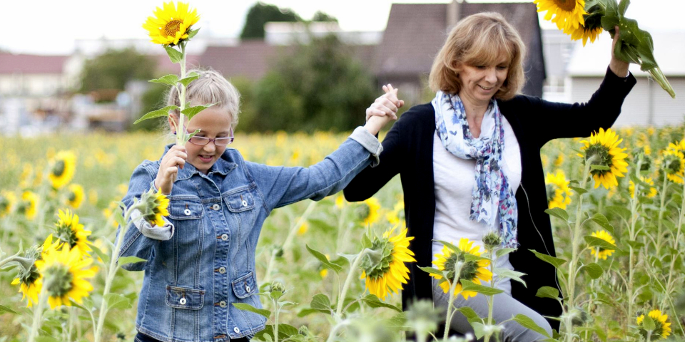 Frau mit Kind in einem Sonnenblumenfeld.